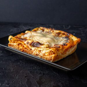 Klasična italijanska lazanja sa slojevima testenine, mesnog i bešamel sosa, posuta rastopljenim sirom, servirana na crnom tanjiru